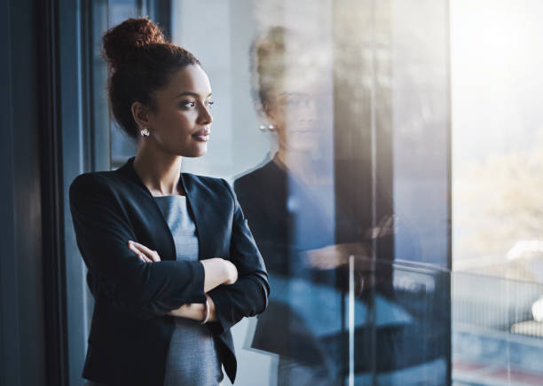 у нее есть амбициозное стремление никогда не сдаваться - women reflection thinking window стоковые фото и изображения