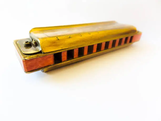 Photo of Old golden diatonic harmonica with ten holes, focused close up on white background and with blur effect.