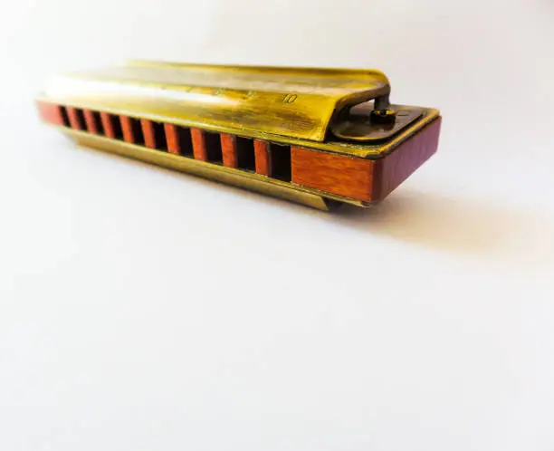 Photo of Old golden diatonic harmonica with ten holes, focused close up on white background and with blur effect.