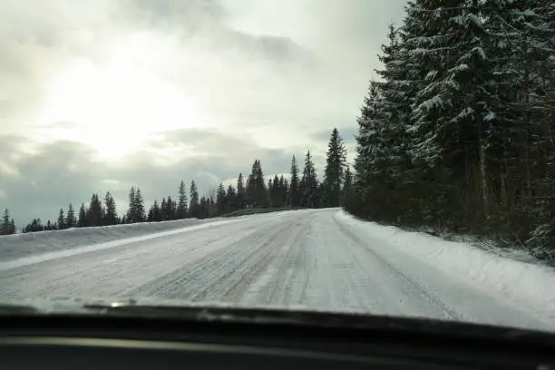 Photo of View from driver's seat on road covered with snow, strong blinding sun back light, risky driving conditions.