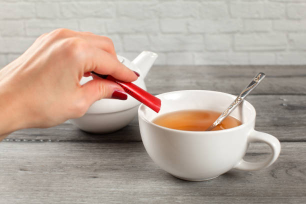 dettaglio sulla mano della donna versando lo zucchero da un piccolo pacchetto in tazza di tè caldo. - gold carbohydrate food food and drink foto e immagini stock