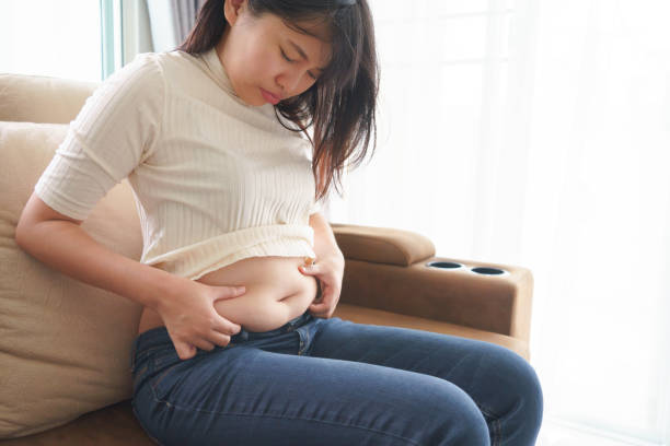 Woman holding her own belly when sitting down on sofa in the living room. stock photo