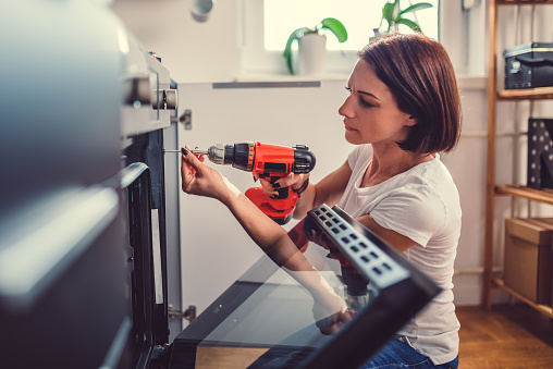 Woman working on a new kitchen installation and using a cordless drill