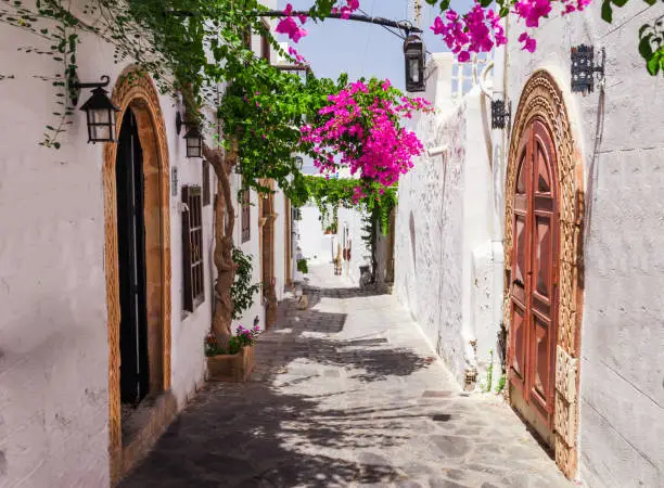 Narrow street in Lindos town on Rhodes island, Dodecanese, Greece. Beautiful scenic old ancient white houses with flowers. Famous tourist destination in South Europe