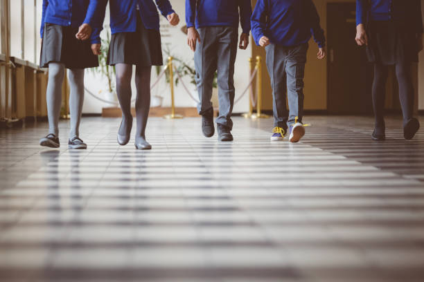 Group of students walking through school hallway Cropped image of school kids in uniform walking together in a row through corridor. Focus on legs of students walking through school hallway. unrecognizable person stock pictures, royalty-free photos & images