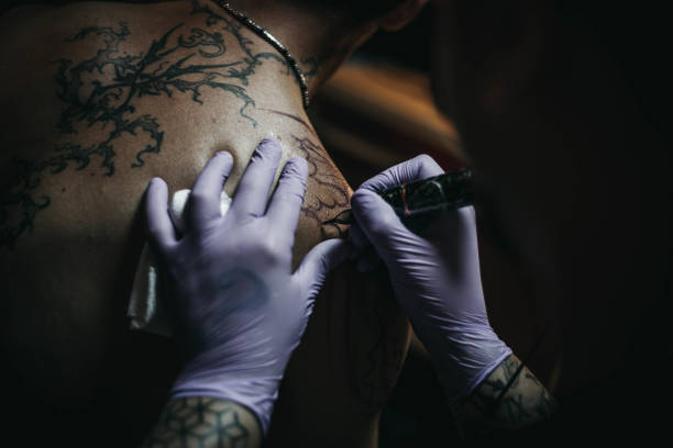 Tattoo artist making tattoo on a men’s shoulder Tattoo artist making tattoo on a men’s shoulder shoulder tattoo designs for men stock pictures, royalty-free photos & images