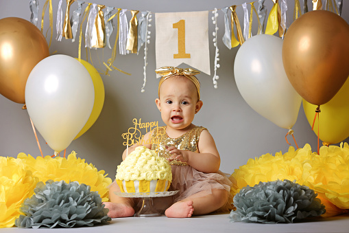 Smiling baby girl celebrating her first birthday, eating cake