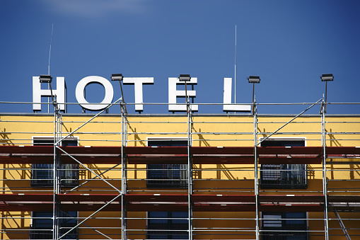A hotel facade with a sign is being renovated and scaffolding is in front of it.