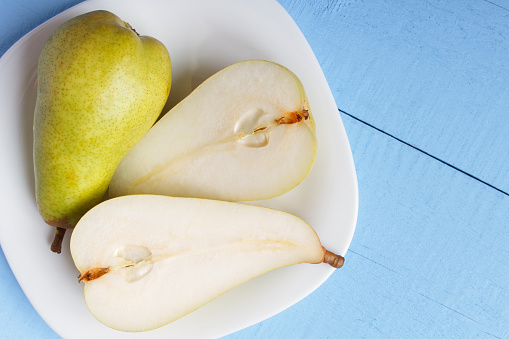 Pears on white plate in closeup. View from above on wooden table. Copy space. Healthy vegetarian food concept.