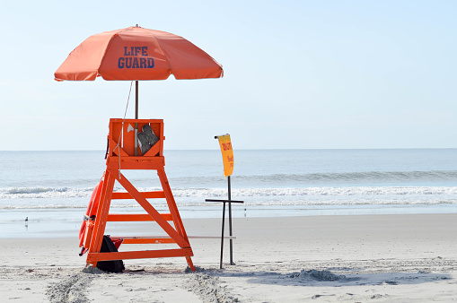 Empty, orange lifeguard chair and umbrella on the beach shore with no people