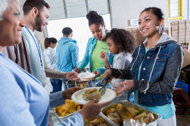 若い女性がフード ドライブ中に食事を提供しています - homelessness food in a row people ストックフォトと画像