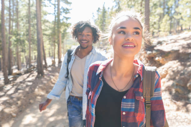 Young woman leads boyfriend down wooded hiking trail