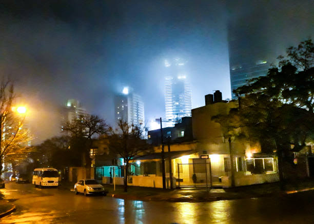 View of the night city in the fog. Street lights in a residential area on a foggy night. View of the windows of multi-storey buildings at night in the fog.