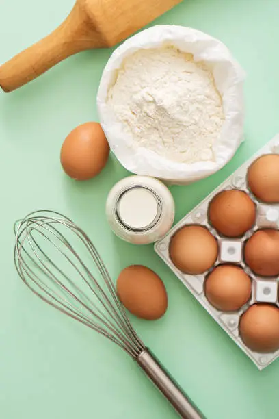 milk, eggs, flour and kitchen tools on green table