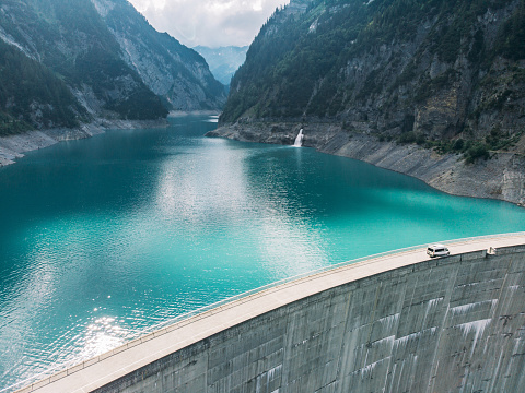 Aerial view of white camper van crossing dam in Swiss Alps