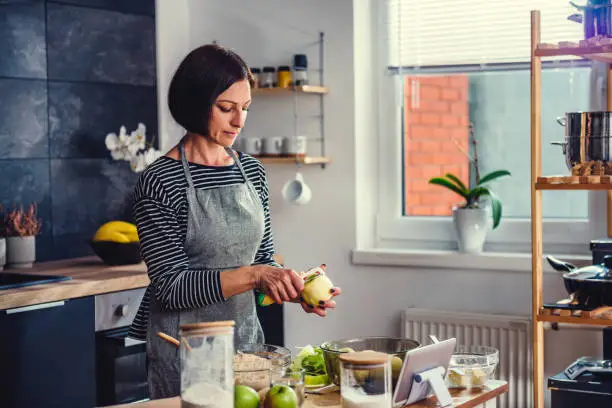 Woman standing in the kitchen by the wooden table and peeling apples