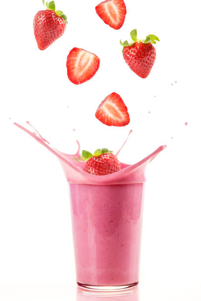 Delicious strawberries falling into a glass of strawberry milkshake stock photo