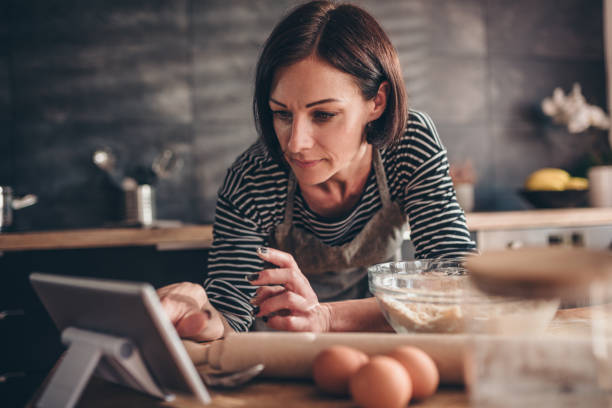 женщина ищет рецепт яблочного пирога на планшете - cooking thanksgiving women baking стоковые фото и изображения