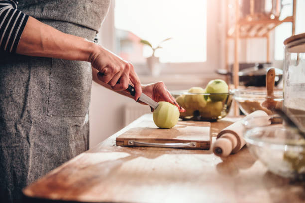 Woman cutting apples in the kitchen Woman standing in the kitchen by the wooden table and cutting apples woman making healthy dinner stock pictures, royalty-free photos & images