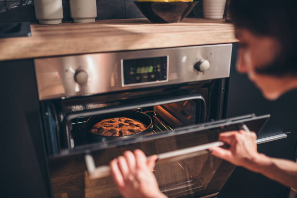 woman checking apple pie in oven - oven imagens e fotografias de stock