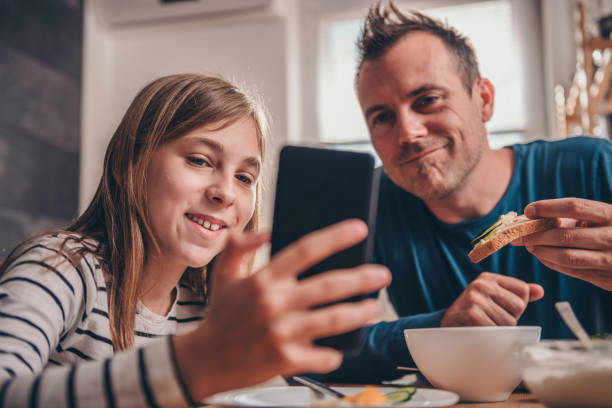 daughter showing video on smart phone to a father - breakfast eating people teens imagens e fotografias de stock