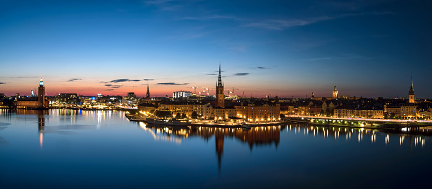 Panoramic view over old town of Stockholm in the evening. Bright city lights reflected in the water. Summer night in Sweden, beautiful skyline of popular travel destination during blue hour