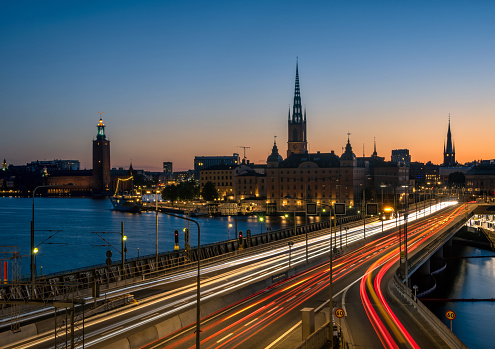Light trails on a bridge to Stockholm at night. Silhouettes of old town against clear evening sky. Long exposure urban cityscape