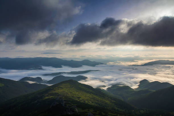 istock Fantastic view of mountain valley covered with low white puffy like snow clouds stretching to foggy horizon under bright morning sky with light orange glow at sunrise. Beauty of nature concept. 1004546338