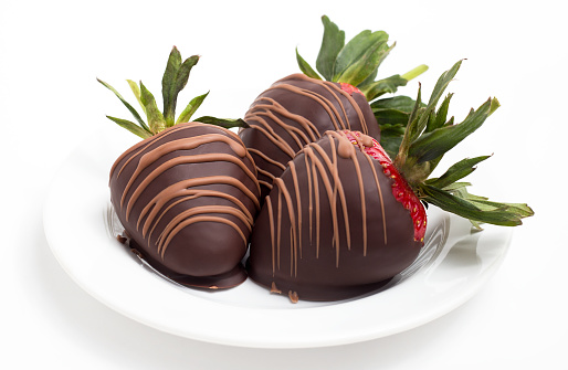 Close up of three chocolate covered strawberries on a white plate