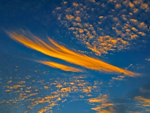 A spectacular  brightly coloured atmospheric Orange and Blue cloudy sky cloudscape featuring a Altocumulus and Cirrus cloud formation in a mid blue sky. New South Wales, Australia.