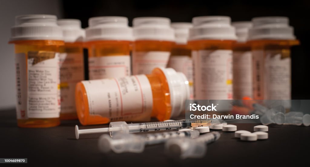 Loaded Syringe and Opioids An injectable drug is loaded into a syringe while prescription medication is strewn about haphazardly. Fentanyl Stock Photo