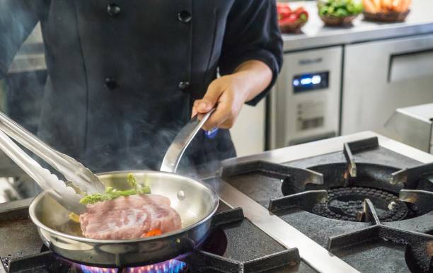 close-up de uma refeição a ser preparada em um fogão industrial por um chef profissional feminino na cozinha de um restaurante nas filipinas. sem rosto é visível. - food tong - fotografias e filmes do acervo