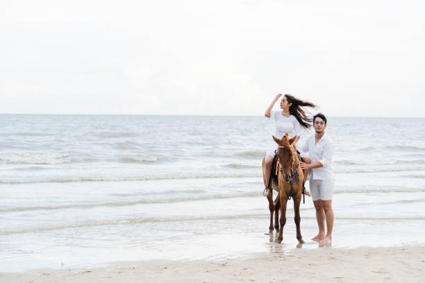 Young couple goes horse riding on tropical beach.