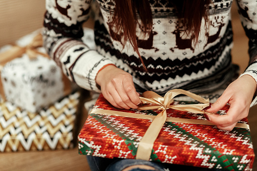 woman in sweaters with deers openning christmas presents under tree closeup. stylish gift ideas. seasonal greetings concept. joyful moment. space for text