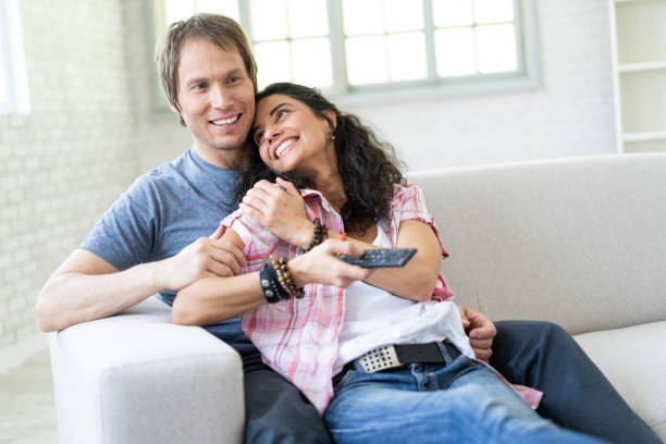 istock Couple sitting on sofa at home and watching TV 1004688504