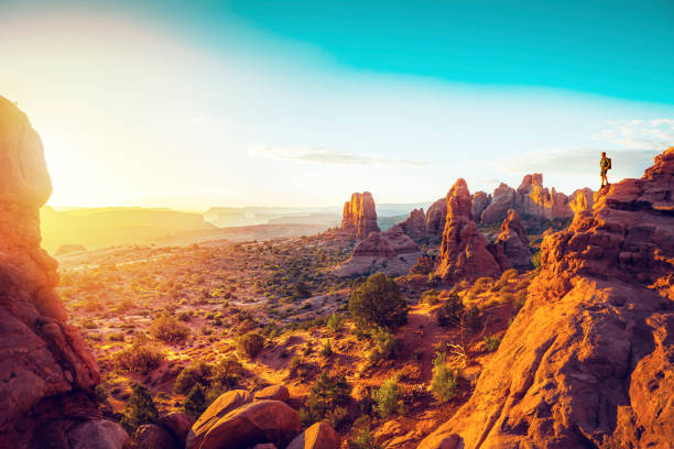 A hiker watching the sunrise from North Window Arch, Utah