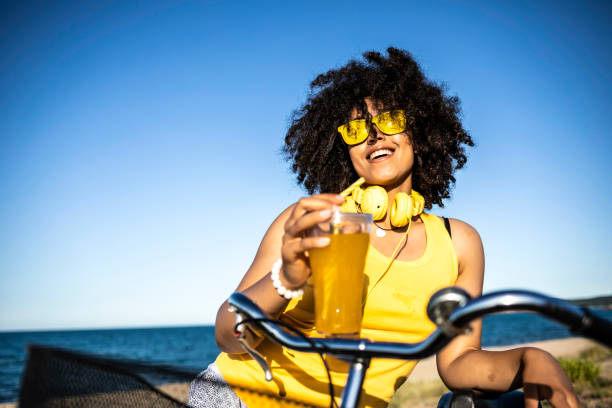istock Cheerful african woman drinking yellow cocktail on beach 1004712158