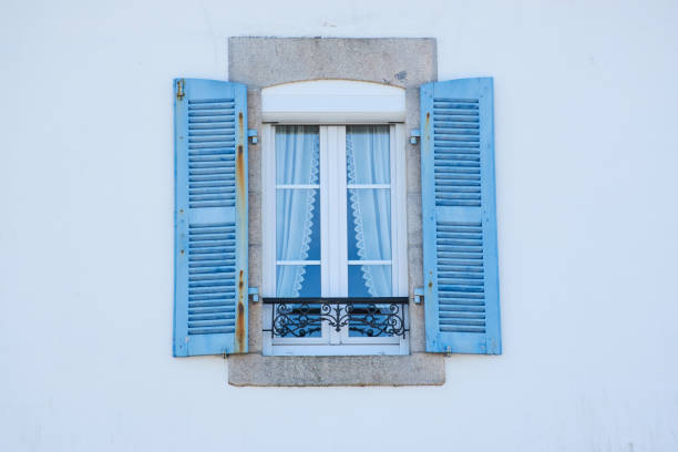 Old window with lace curtains and blue shutters in a house in Brittany, France