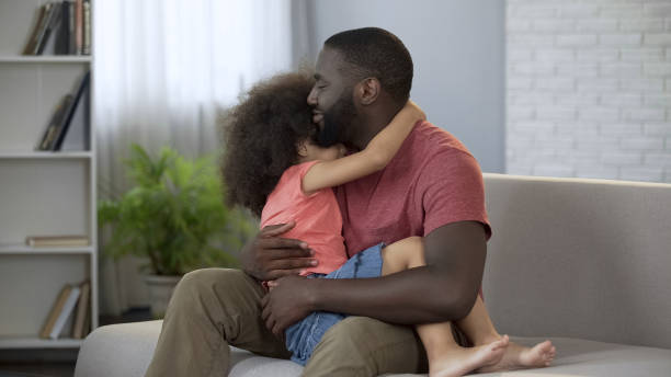 istock Dad holding his little daughter on lap gently hugging her, conscious parenthood 1004734684