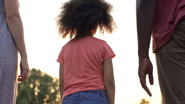 istock Small adopted girl standing between two new parents, afraid to love and trust 1004734996