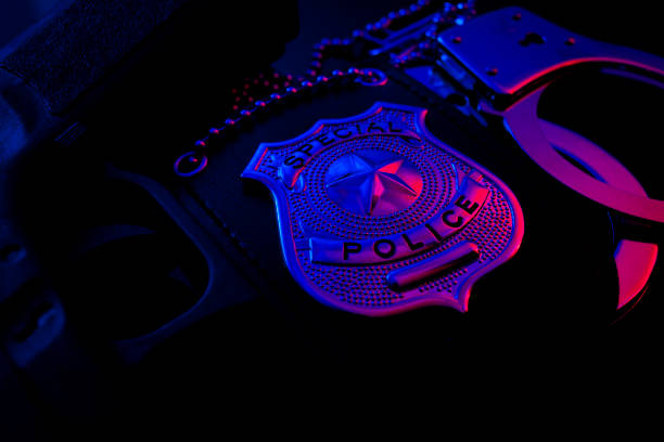 polizei abzeichen, handschellen und pistole nachts im blaulicht - polizeiabzeichen stock-fotos und bilder