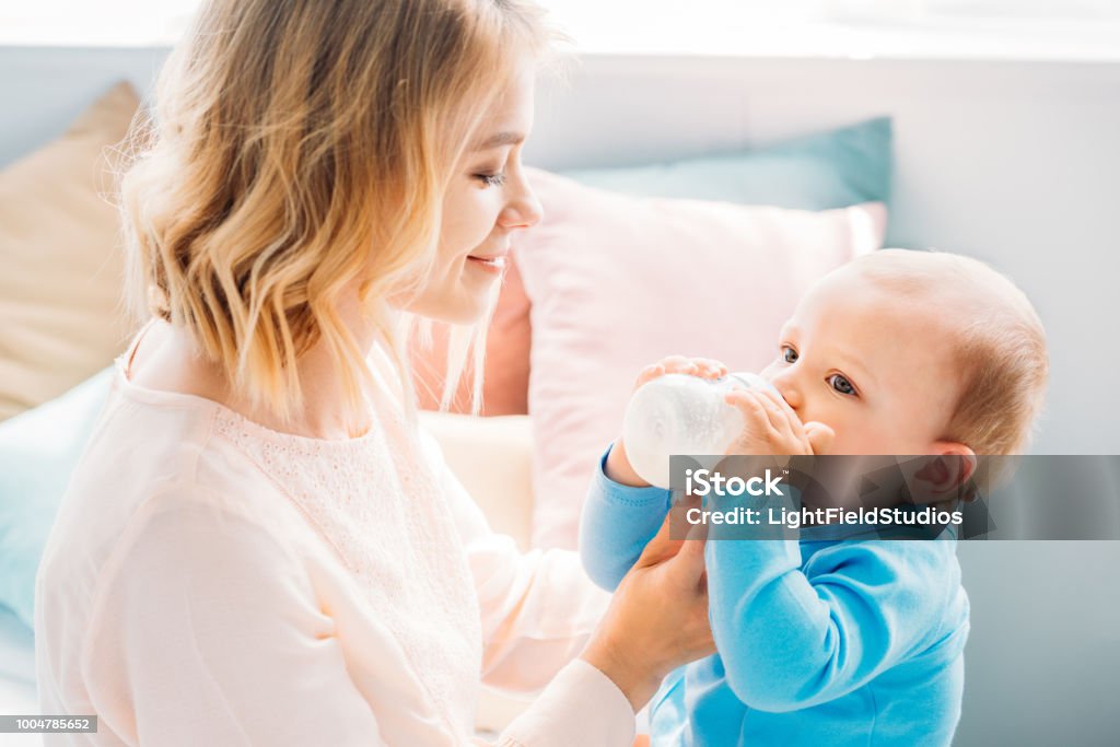 happy mother feeding her little child with baby bottle at home Baby Bottle Stock Photo