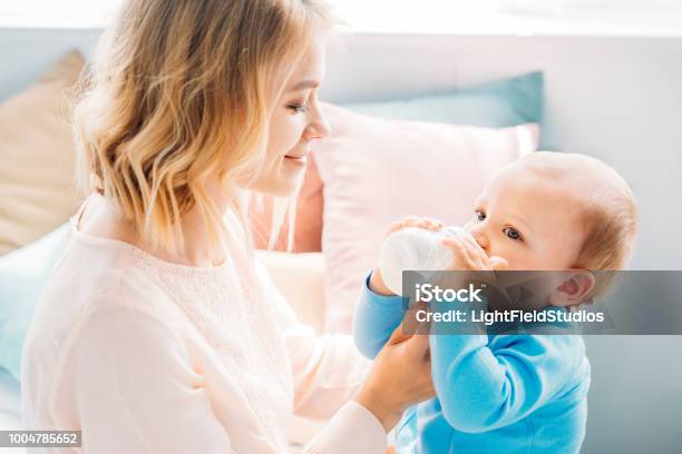 Happy Mother Feeding Her Little Child With Baby Bottle At Home Stock Photo - Download Image Now