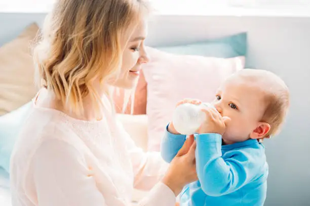 happy mother feeding her little child with baby bottle at home