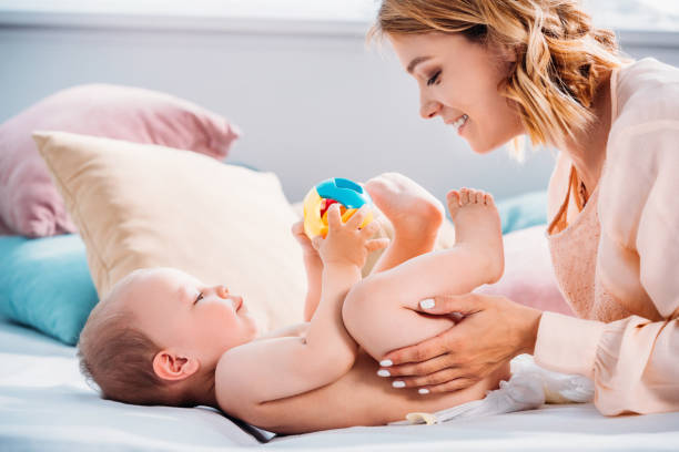 istock happy mother putting diaper on little child while he playing with toy 1004785720