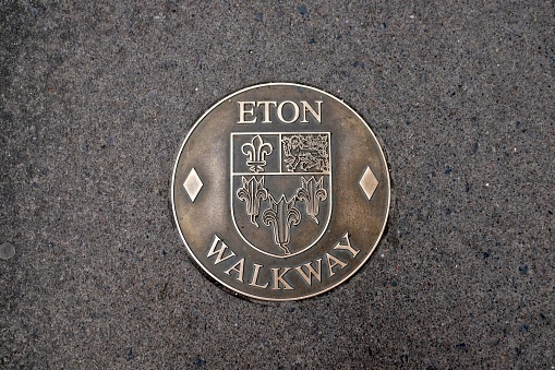 Eton, England - June 9, 2018: the 'Eton Walkway' links eighteen landmarks in the small town of Eton, where the world-famous Eton College is located.  It takes around an hour to walk the two-mile route.  This bronze sign, sunk into the pavement outside Porny School, contains Eton's coat of arms (given to the town by King Henry VI in 1449).