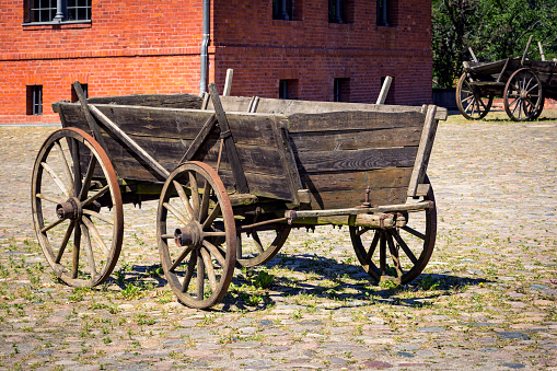 An old historic carriage stands in the yard of a historic farm. In the background stands a manor house made of bricks.