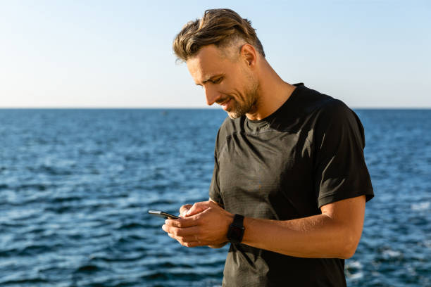 istock smiling adult man using smartphone on seashore 1004830972