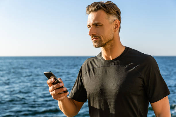 istock handsome adult man with smartphone on seashore and looking away 1004830978