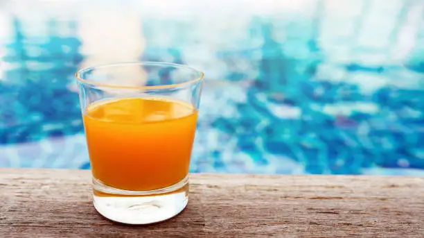Summer Drink at the Swimming Pool. Glass of Orange Juice on the Poolside. Relaxation on Vacation or Holidays Concept